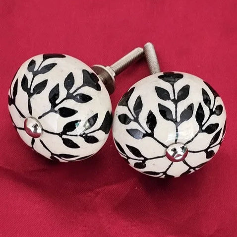 Pair of ceramic knobs with hand-painted black leaf patterns on white surface, ideal for cabinets and dressers – home hardware by Troika.
