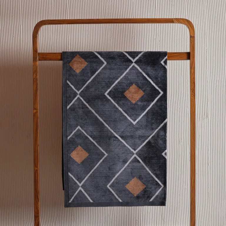 Dark grey dhurrie featuring a diamond pattern with rust-colored centers, displayed on a wooden rack against a textured wall.