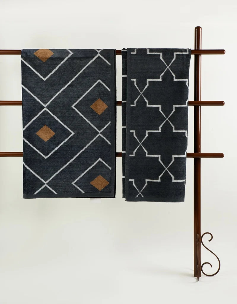 Side-by-side display of two grey dhurries on a rack one with rust diamond motifs and the other with geometric lattice pattern.