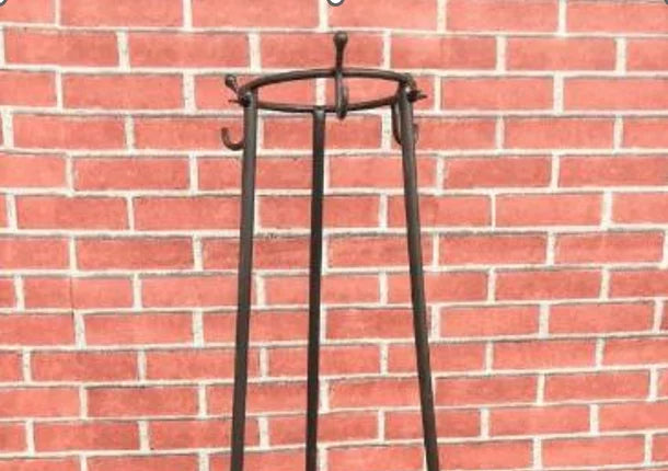 Top portion of a tall iron stand with four legs and hooks at the top, placed against a red brick wall.