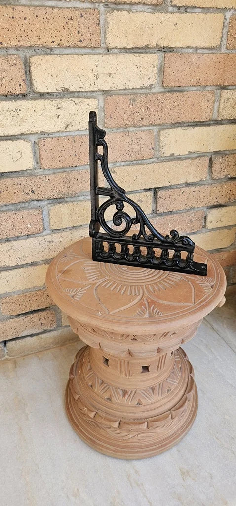 Antique-style wall bracket in iron displayed on terracotta base, perfect for classic decor.