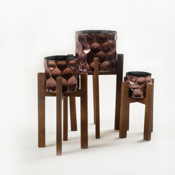 Set of 3 copper finish planters with textured surface displayed on tall solid wood stands for indoor plants.