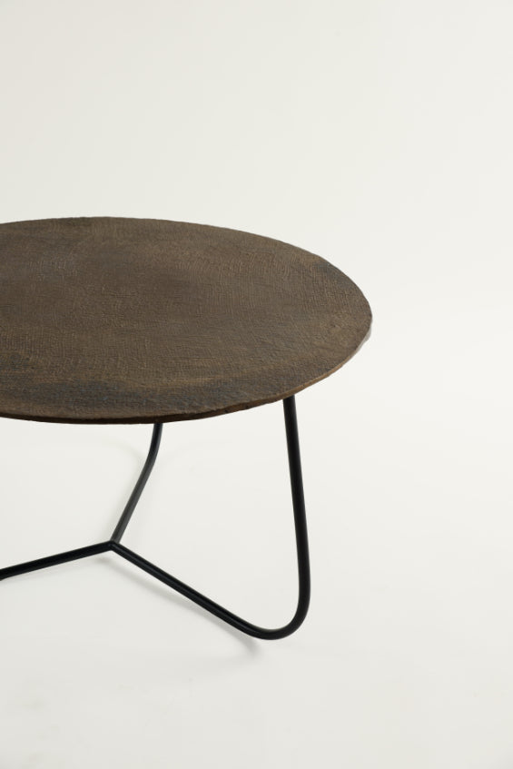 Close-up side view of rustic metal coffee table with earthy finish and curved black legs – artisanal industrial furniture from Troika Life.