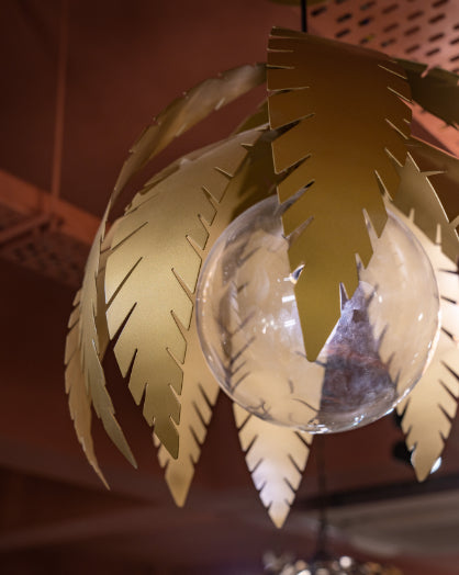 Close-up of Willow Pendant light with gold leaf accents around a central glass globe on warm ceiling backdrop.