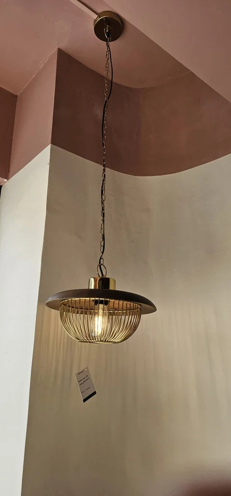 Elegant brass pendant light with a wide disc shade and golden cage housing a bulb, suspended from a black chain – designer ceiling lighting by Troika.