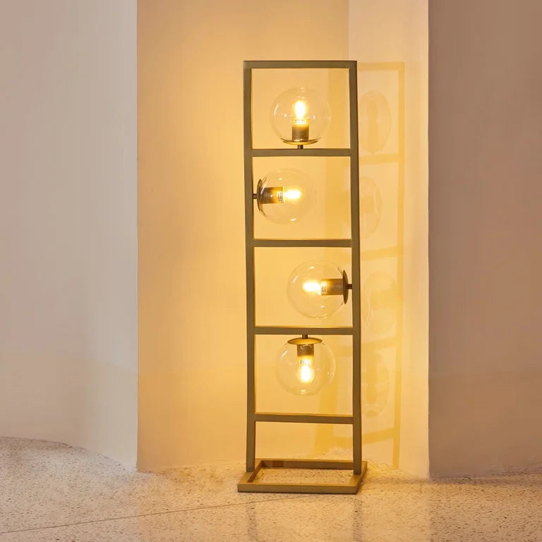 Modern floor lamp with four exposed globe bulbs in a rectangular metal frame, casting warm ambient light – artistic statement lighting by Troika.
