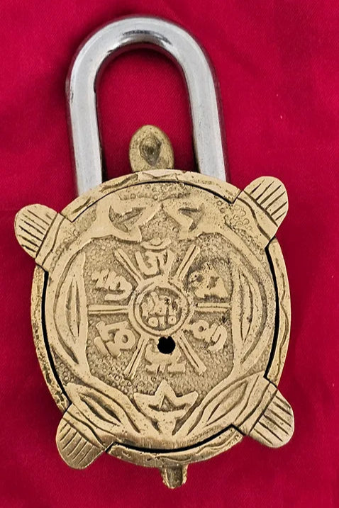 Antique brass turtle-shaped padlock with engraved Sanskrit design on red background