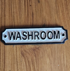 Classic black and white cast iron washroom signplate mounted on wooden surface.