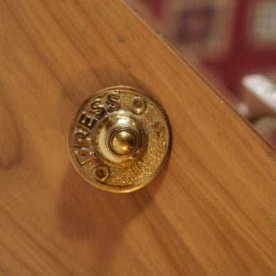 Vintage-style brass doorbell with engraved 'Press' text, mounted on wooden surface – antique finish hardware accessory from Troika.