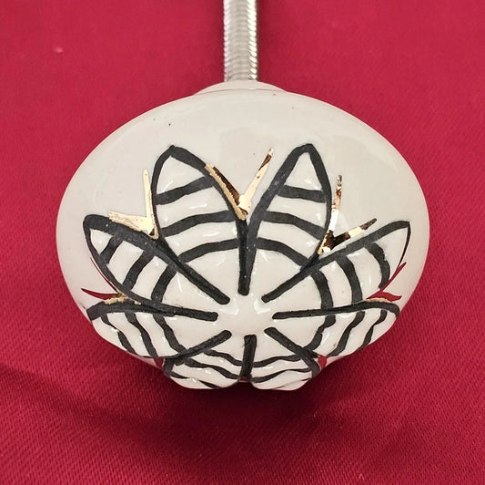 Single ceramic drawer knob with black striped petal design and golden accent on a white base – handcrafted home hardware by Troika.