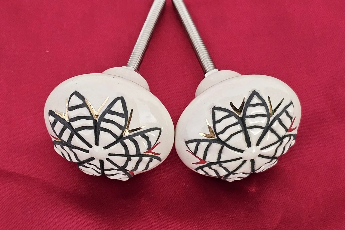 Pair of ceramic knobs featuring cone flower design in black and gold on white background – decorative cabinet handles by Troika.