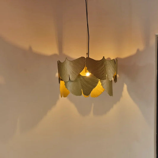 Pendant light made of overlapping brass ginkgo leaves. Emits warm light with unique shadows, perfect for ambient lighting.