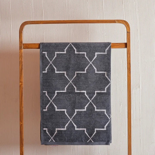 Dark grey dhurrie featuring a silver geometric lattice pattern, displayed flatly against a textured white wall.