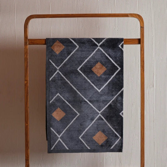 Dark grey dhurrie featuring a diamond pattern with rust-colored centers, displayed on a wooden rack against a textured wall.