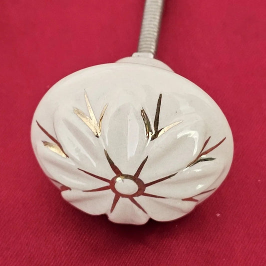 Ivory ceramic knob with gold and brown petal accents, shaped like a flower, set on a red background.