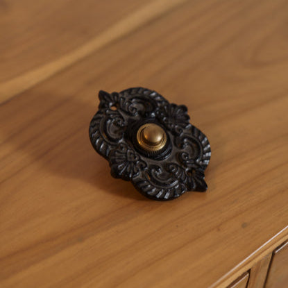Ornate oval black iron doorbell with antique brass button vintage-style hardware for doors and gates.