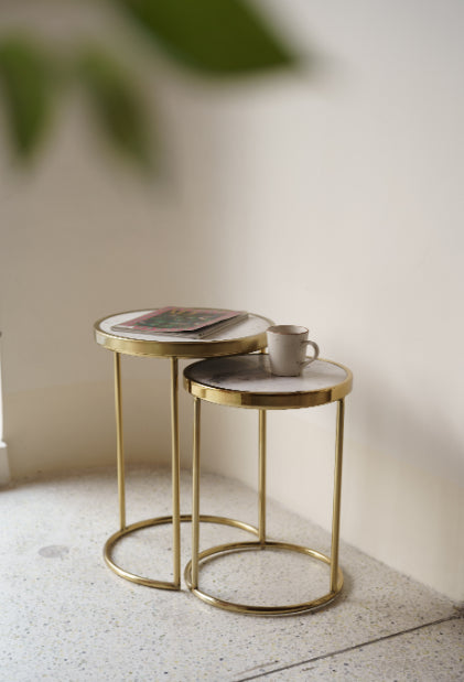 Gold frame nesting tables with marble top styled with magazine and ceramic mug.