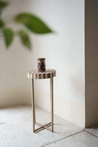Radius side table with vertical wood stripes and brass legs, placed in a minimalist corner with a decorative jar – Troika Life modern furniture.