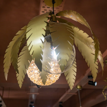 Willow Pendant Light with golden palm-shaped blades and a central bulb, suspended from the ceiling in warm décor.