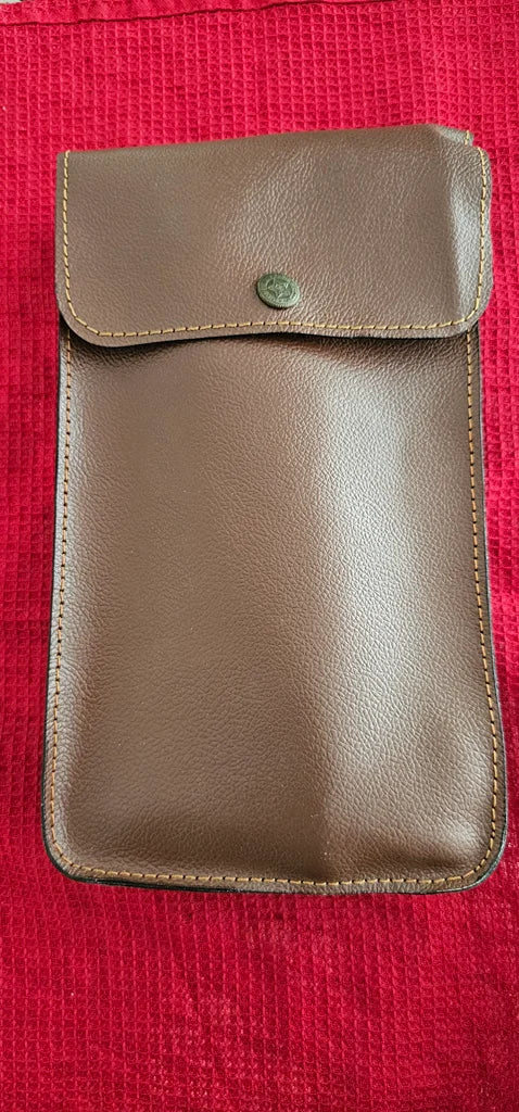 Brown leather pouch with button flap, laid on red textured fabric – bar tool storage case from Troika.