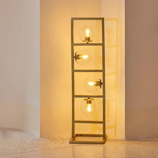 Modern floor lamp with four exposed globe bulbs in a rectangular metal frame, casting warm ambient light – artistic statement lighting by Troika.