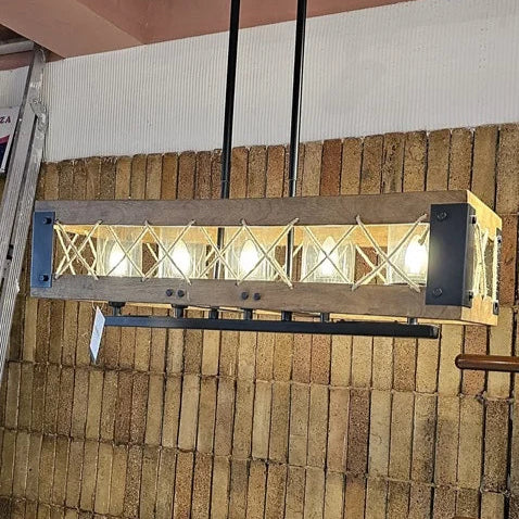 Rectangular wooden frame chandelier with criss-cross rope detailing and exposed bulbs. Ideal for rustic or farmhouse-style interiors. Suspended by two black rods from the ceiling.