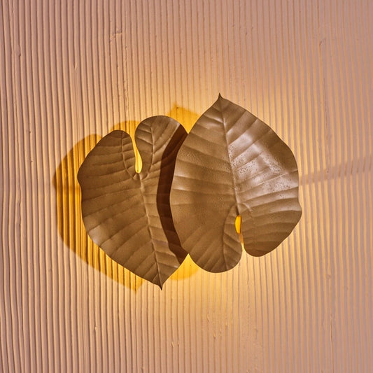 Tropical leaf wall light with dual overlapping metal leaves casting soft ambient glow on textured wall